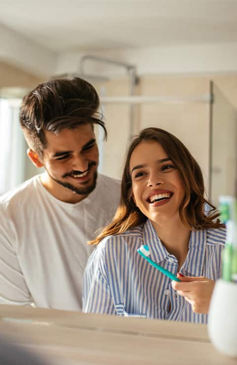 pareja sonriendo mientras usa cepillos de dientes colgate pareja sonriendo mientras usa cepillos de dientes colgate
